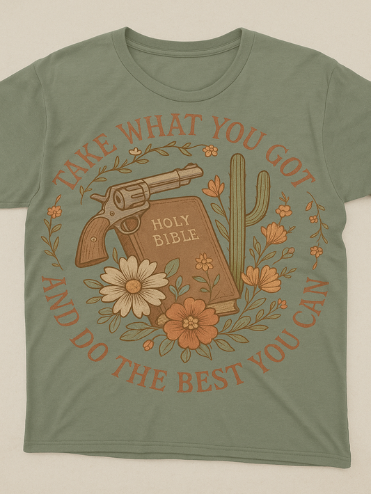 Green t-shirt with graphic design featuring a Bible, revolver, cactus, and flowers on a beige background.